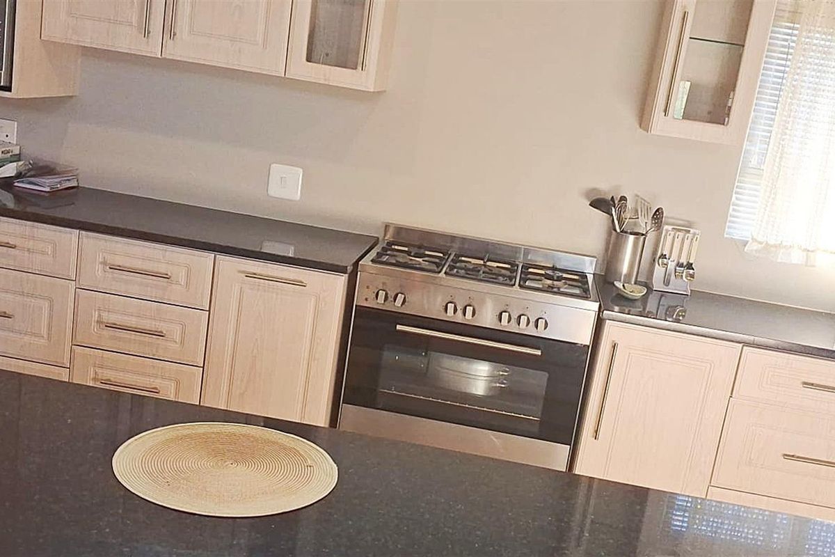 A functional kitchen featuring light wood cabinetry, dark granite countertops, and a built-in stainless steel gas stove and oven combination.