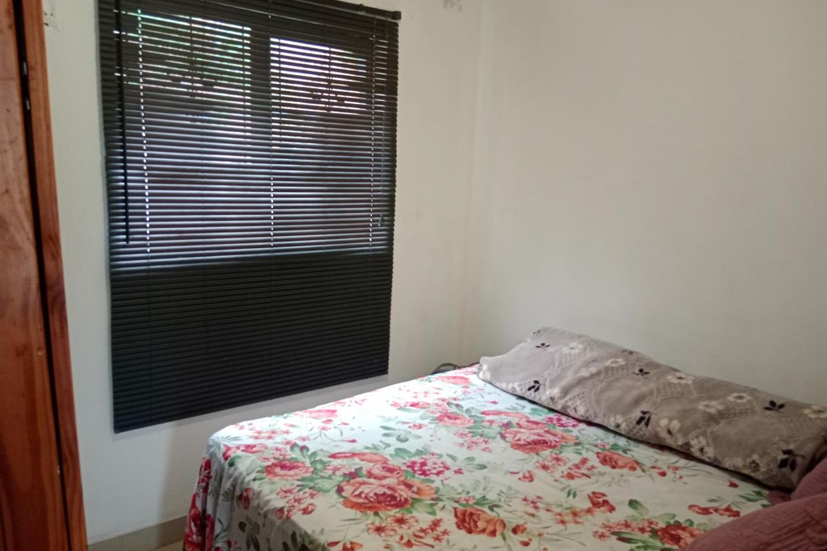A functional bedroom featuring a window with fitted dark venetian blinds and tiled flooring.