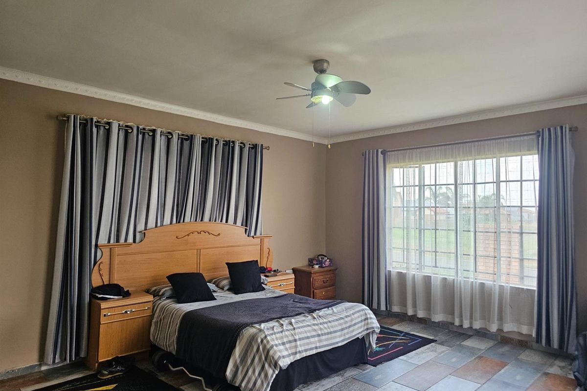 Spacious bedroom featuring tiled flooring, decorative ceiling cornices, and a ceiling fan, offering ample natural light through large windows.