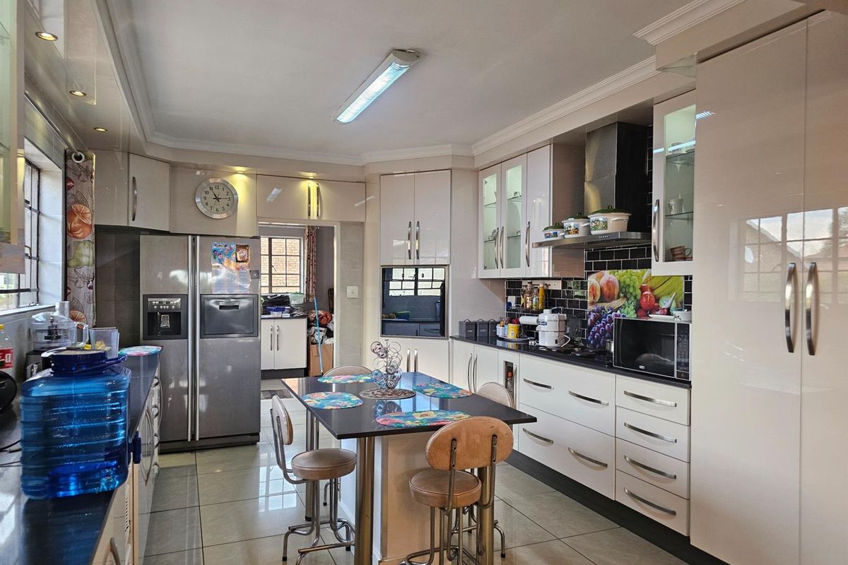 Modern kitchen featuring high-gloss cabinetry, integrated oven, extractor fan, and a central breakfast island with tiled flooring throughout.