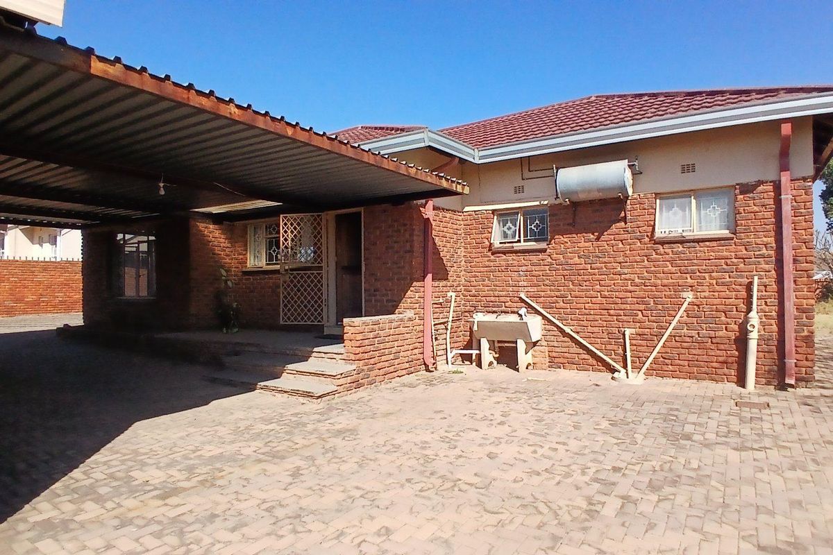 Exterior view of a brick house featuring a covered carport, paved driveway, and external utility area with a concrete wash trough.