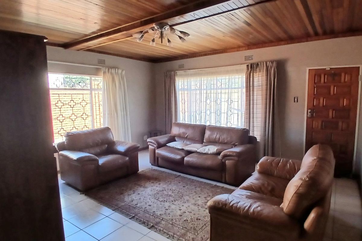 A spacious living room featuring a timber-clad ceiling, tiled flooring, and large windows with security bars, providing a traditional and functional living space.