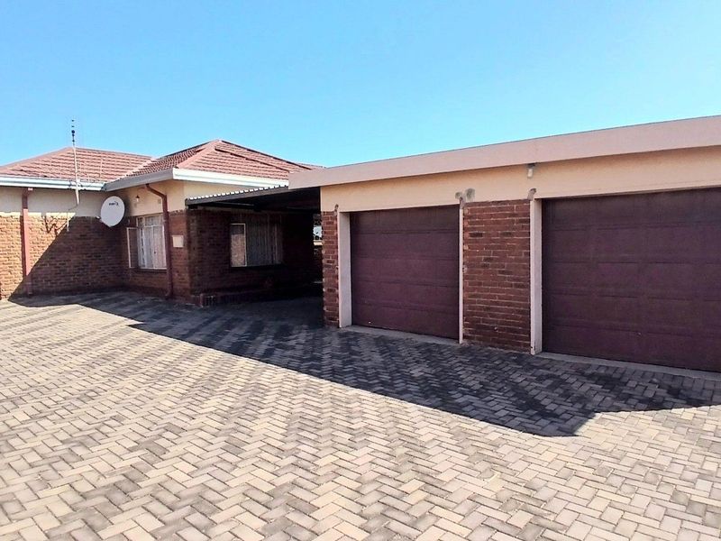Front exterior view of a brick house featuring a paved driveway and a double garage with sectional doors.