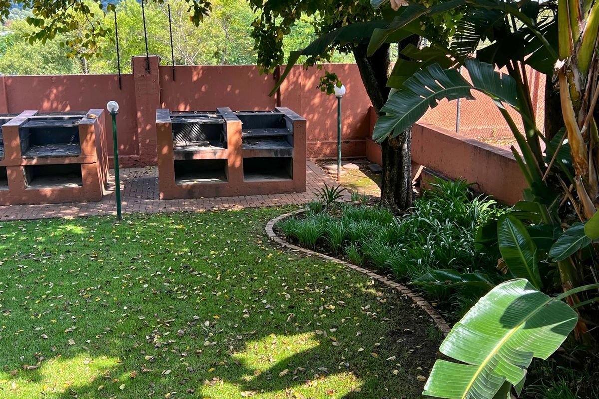 Outdoor entertainment area featuring dual built-in brick braai stations, paved flooring, and established garden landscaping with perimeter walling.