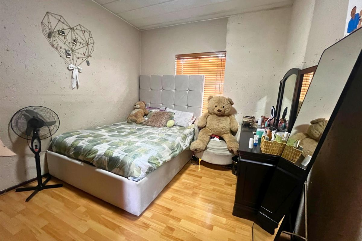 A bedroom featuring wood-look laminate flooring, a window with fitted blinds, and textured wall finishes.
