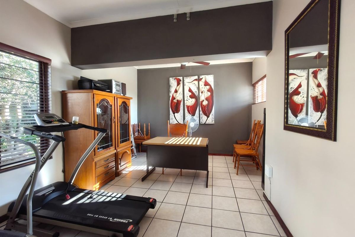 A multi-purpose room featuring tiled flooring, a large bulkhead ceiling detail, and window blinds, currently utilized as a home office and gym space.