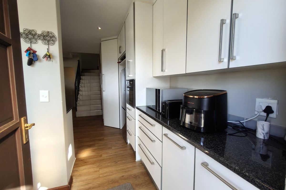 A modern kitchen featuring white cabinetry, dark granite countertops, and integrated appliances, leading towards a staircase in the background.