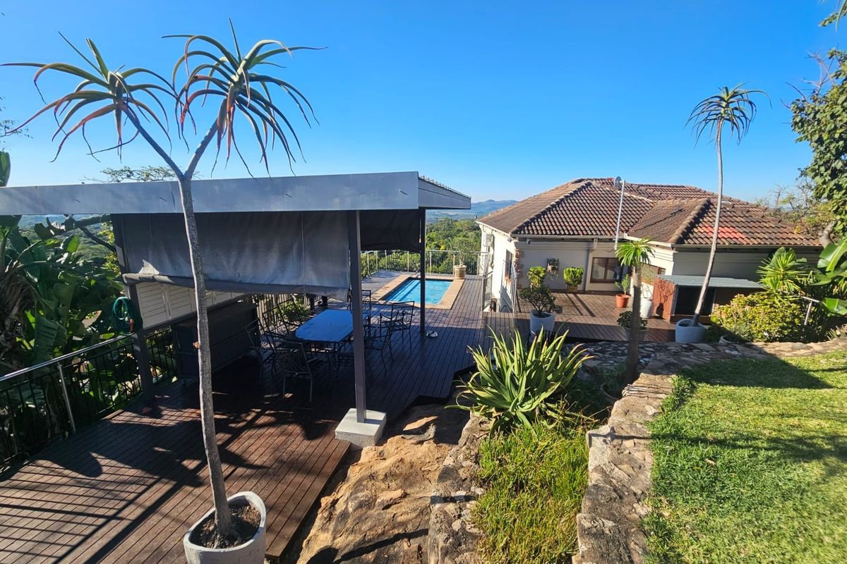 Elevated view of the rear exterior featuring a timber deck, covered patio area, swimming pool, and landscaped garden with scenic horizon views.