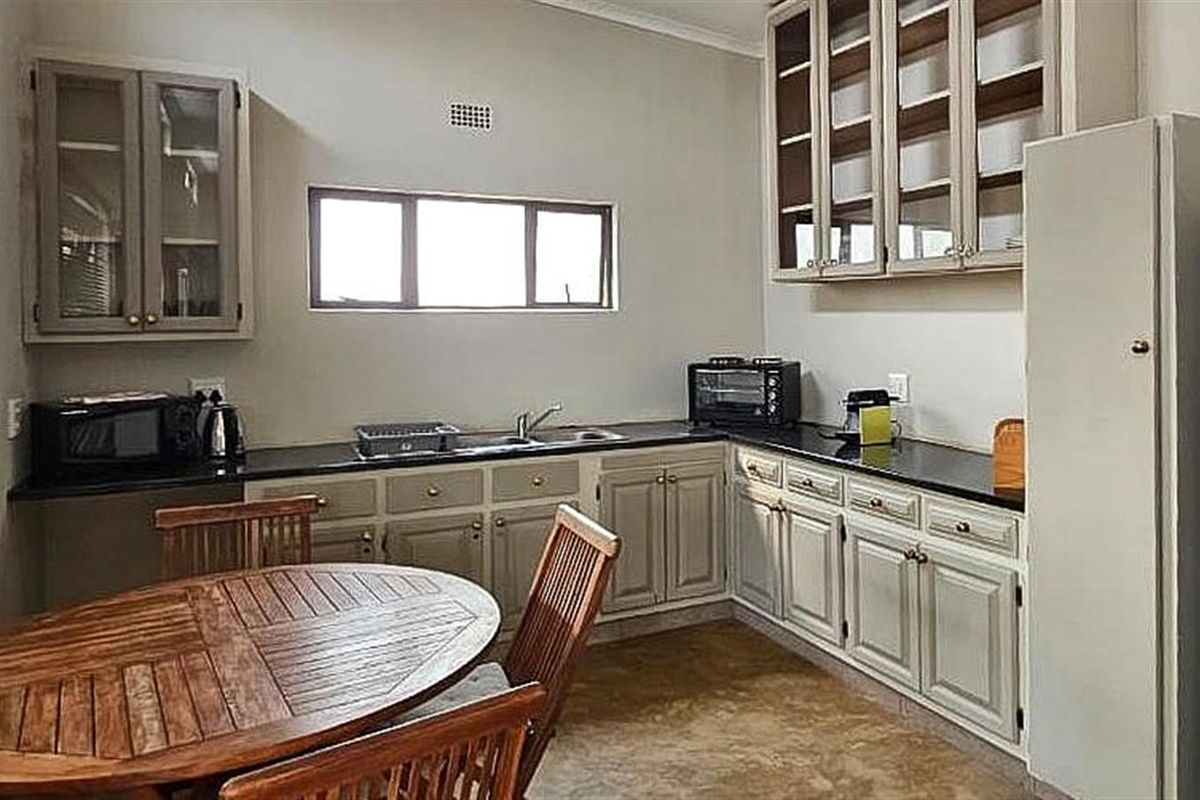 A functional kitchen featuring light-toned cabinetry, dark countertops, a double sink, and ample upper storage, with an integrated dining area.