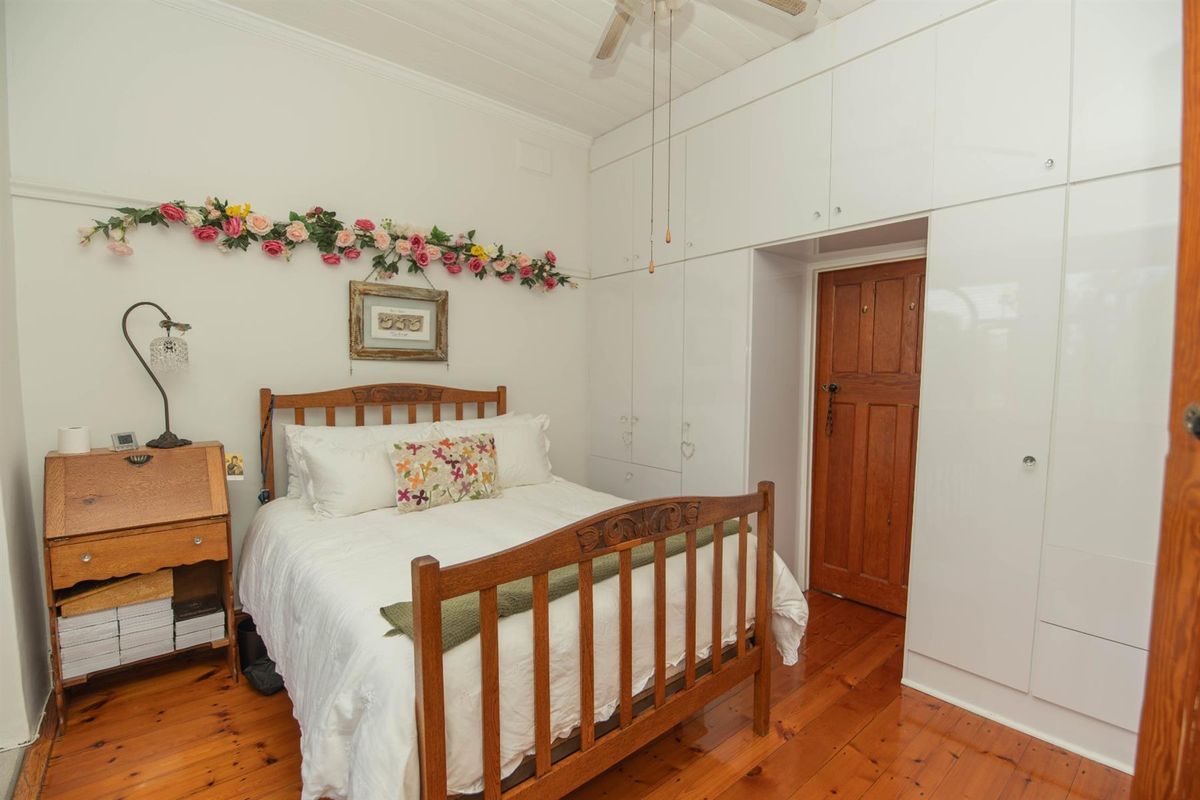 A bedroom featuring polished timber flooring, white tongue-and-groove ceiling, and extensive floor-to-ceiling built-in cabinetry.