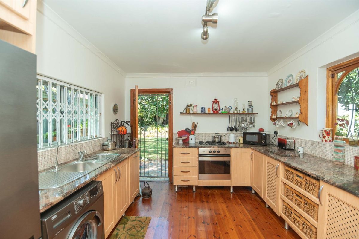 A functional kitchen featuring light wood cabinetry, granite countertops, a built-in oven and hob, and direct access to the rear garden.