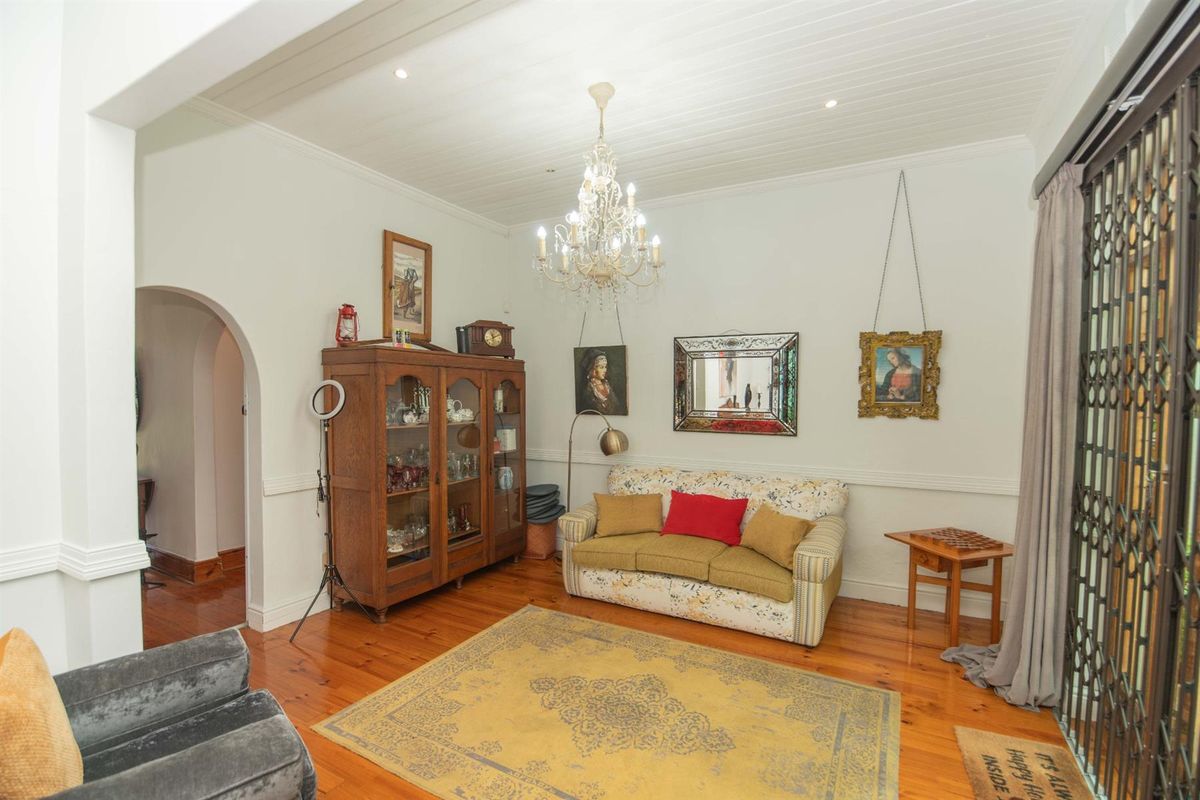 A cozy living room featuring polished timber flooring, a classic chandelier, and an arched doorway leading to adjacent living spaces.