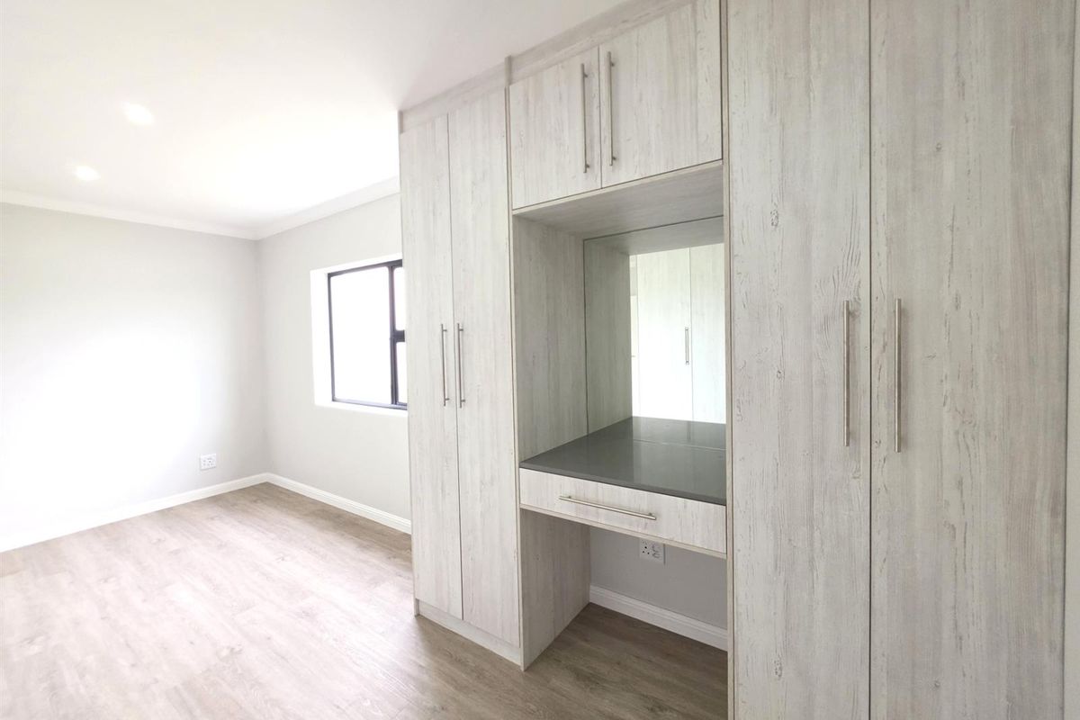 A bright bedroom featuring modern light wood-grain built-in cupboards with an integrated vanity station and durable laminate flooring.
