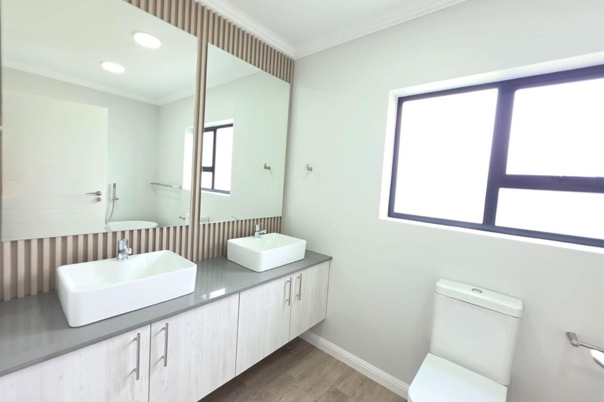 Modern bathroom featuring a double vanity with vessel sinks, stone countertop, large mirrors, and a contemporary toilet.