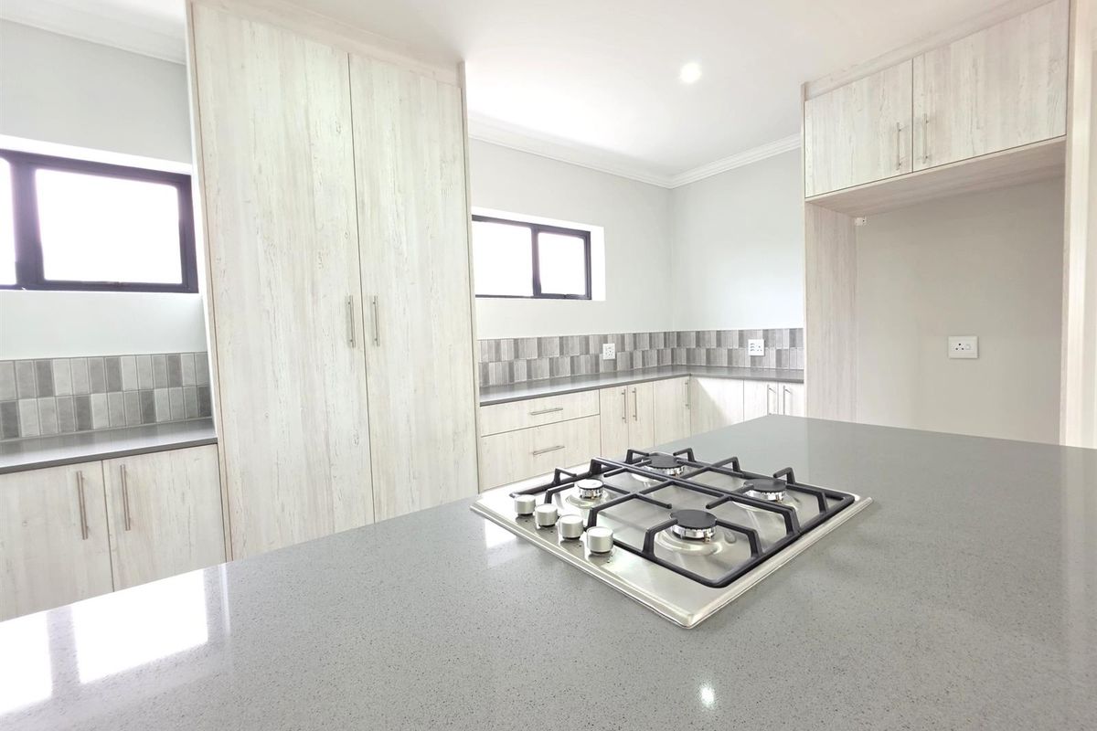 Modern kitchen featuring light wood-grain cabinetry, grey stone countertops, a central island with a built-in gas hob, and tiled splashbacks.