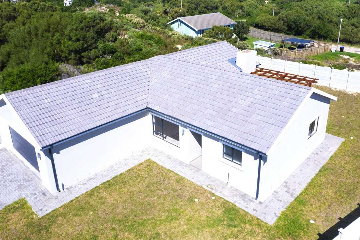 Aerial view of a modern single-story house featuring a tiled roof, paved driveway, attached garage, and a surrounding garden area.