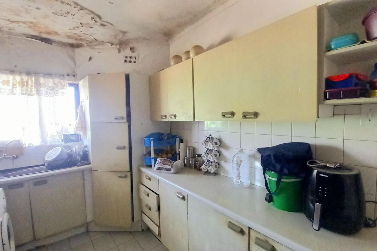 A dated kitchen featuring built-in cabinetry, tiled splashbacks, and a sink, currently requiring significant ceiling repairs and general refurbishment.
