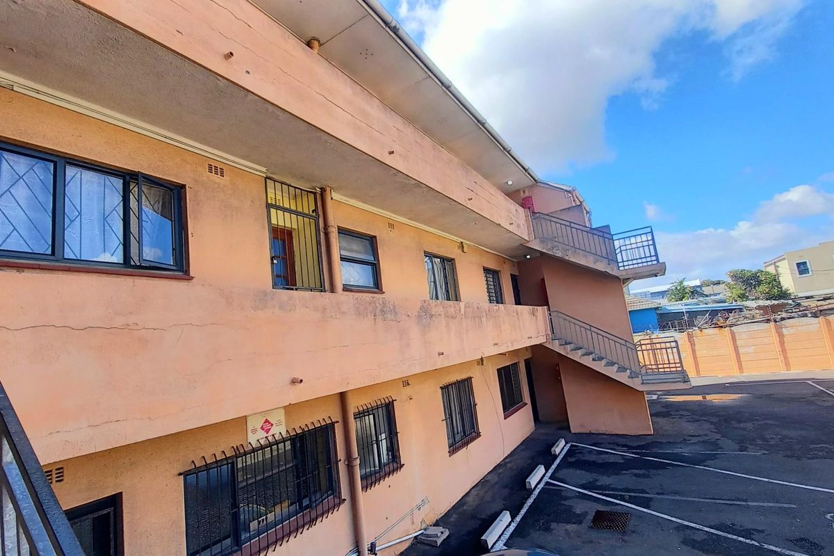 Exterior view of an apartment building featuring a concrete staircase, metal security bars on windows, and paved parking area.