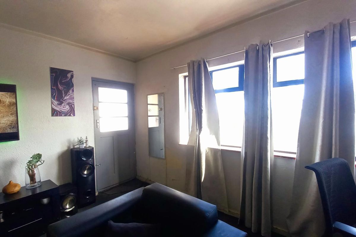 A living room area featuring large windows with curtains, a solid entrance door, and neutral wall finishes.