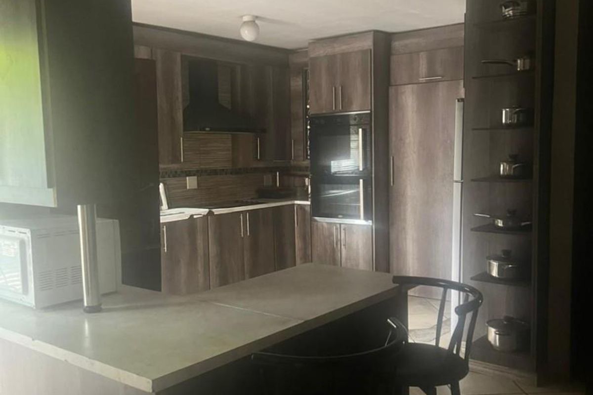 A functional kitchen featuring dark wood-look cabinetry, a built-in double oven, an extractor fan, and a breakfast bar counter with tiled flooring.
