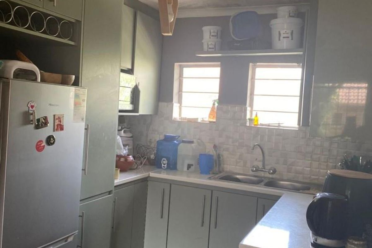 Compact kitchen featuring sage green cabinetry, double sink, tiled backsplash, and laminate flooring, with visible ceiling maintenance required.