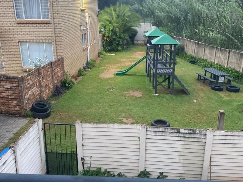A view of a communal garden area featuring a lawn, brick boundary walls, and a precast concrete fence, viewed from an elevated balcony.