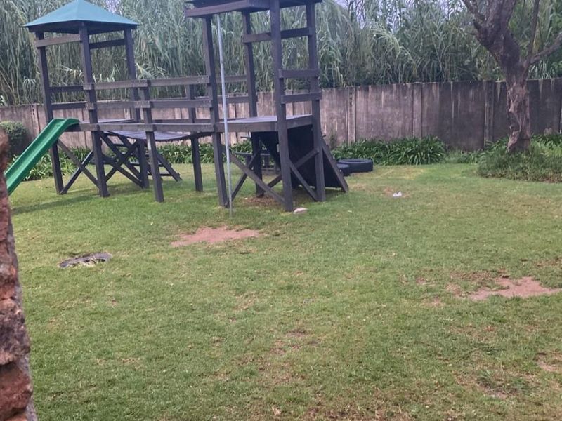 A private garden area featuring a wooden playground structure and a perimeter wall, offering potential for landscaping and outdoor improvement.