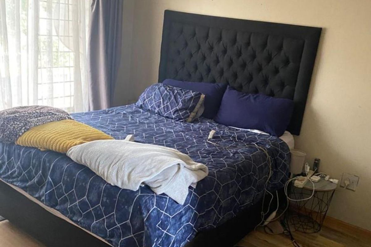 A bedroom featuring laminate flooring and a sliding door with security gate access, providing natural light and ventilation.