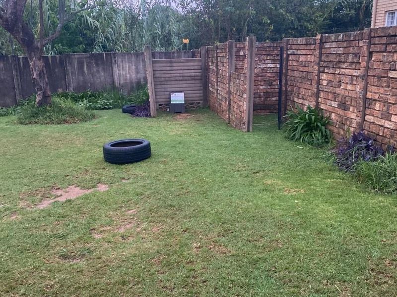 A private garden area featuring a brick boundary wall, concrete fencing, and established trees, offering potential for landscaping and outdoor improvement.
