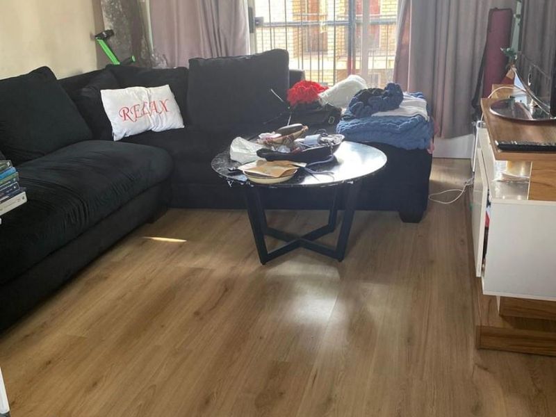 A living room featuring laminate flooring and a sliding glass door with an integrated security gate, providing access to the exterior.