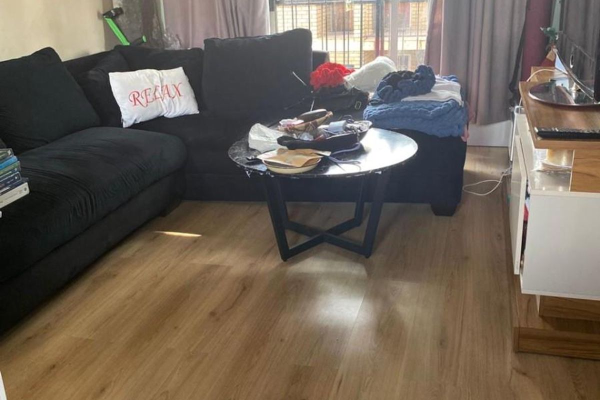 A living room featuring laminate flooring and a sliding glass door with an integrated security gate, providing access to the exterior.