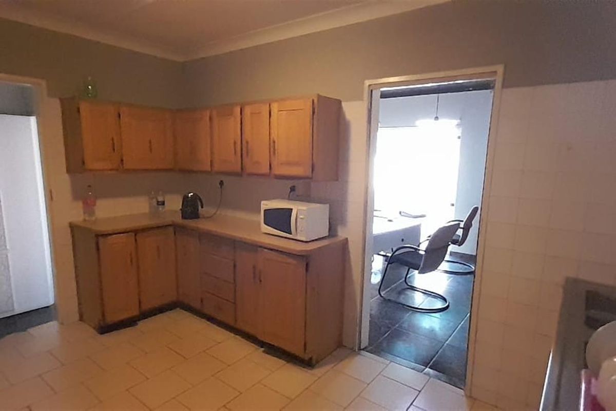 A functional kitchen featuring wooden cabinetry, tiled flooring, and a practical layout with direct access to an adjacent living area.