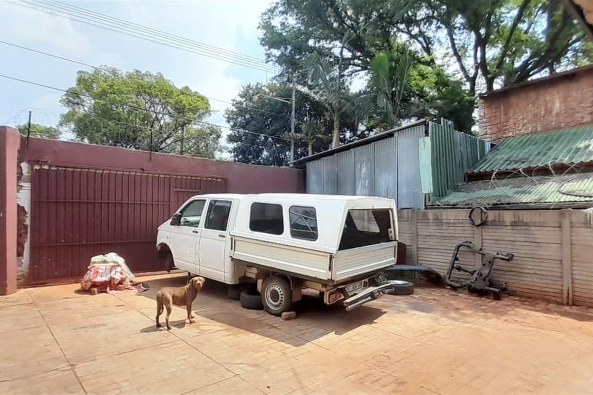An outdoor paved yard area featuring high boundary walls, security fencing, and a large metal gate entrance.
