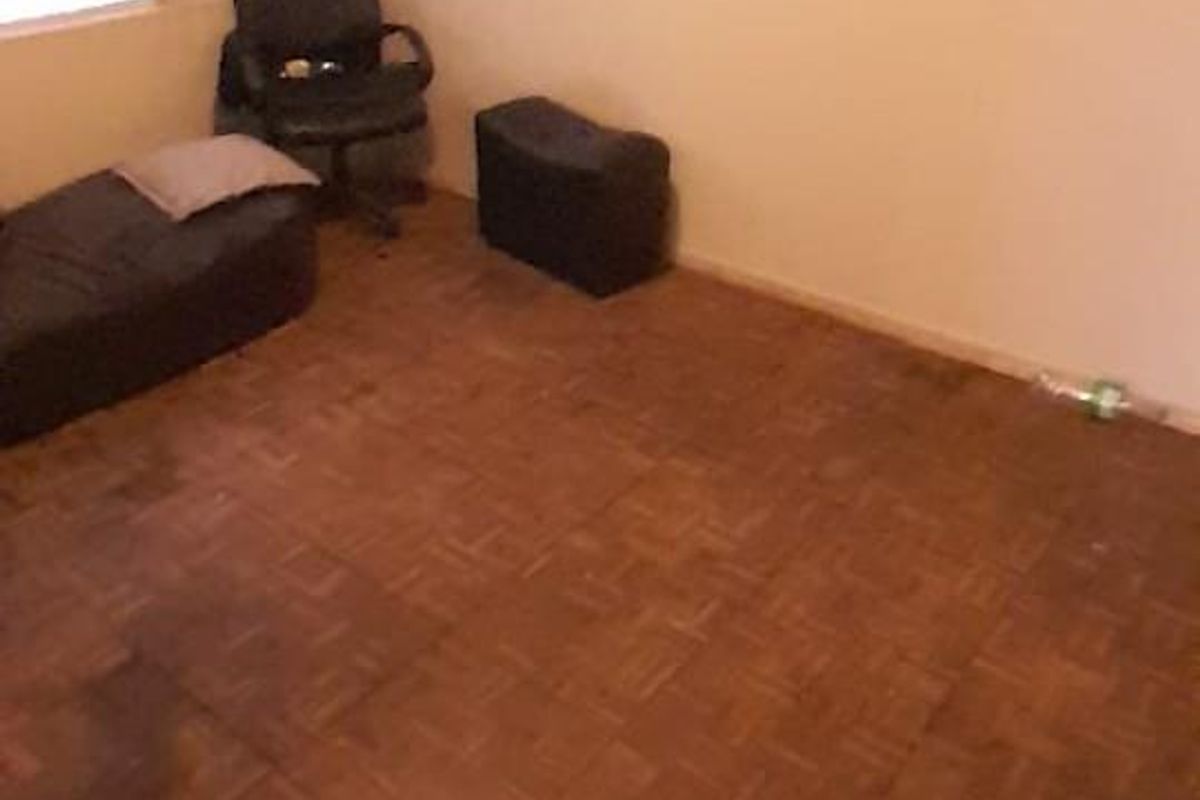 A bedroom featuring traditional parquet wood flooring and a window with security bars.
