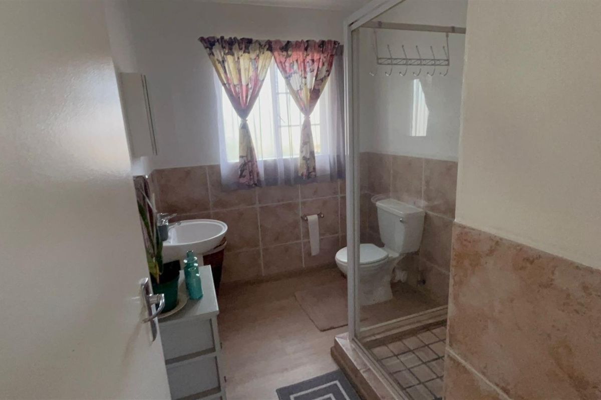 A functional bathroom featuring a pedestal basin, toilet, and a glass-enclosed shower with tiled splashbacks and security bars on the window.