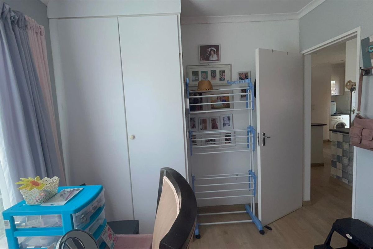 A bedroom featuring built-in wardrobe storage and laminate flooring, with a doorway leading to an adjacent kitchen area.