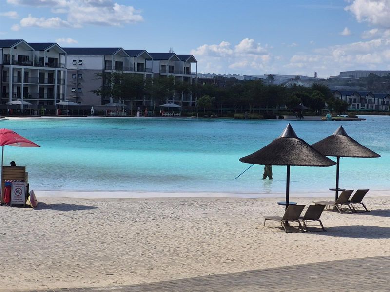 A scenic view of the estate's communal lagoon and sandy beach area, featuring clear turquoise water and surrounding apartment buildings.
