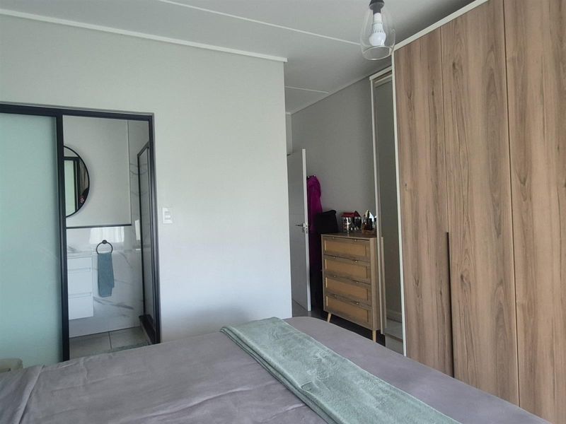 A well-maintained bedroom featuring built-in wooden wardrobes and an en-suite bathroom with modern finishes.