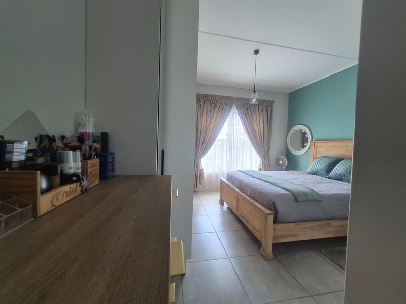 A bedroom featuring tiled flooring, a feature wall, and built-in cupboard space, viewed from an adjacent hallway.