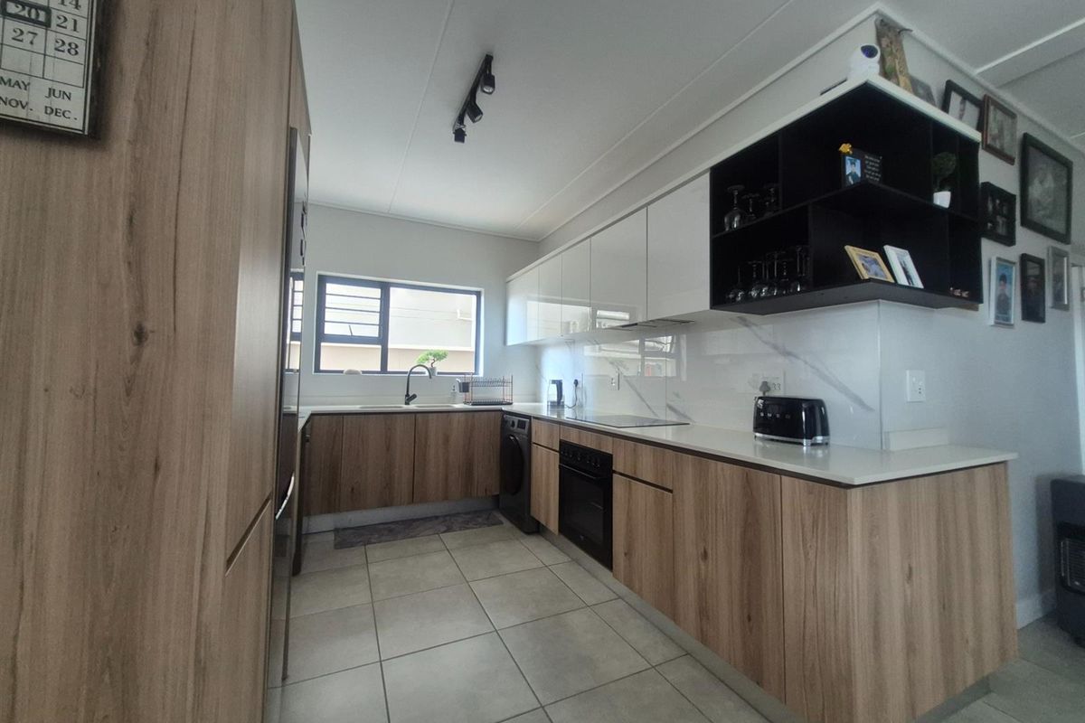 Modern kitchen featuring wood-grain cabinetry, white stone countertops, integrated oven, hob, and a sleek marble-look splashback with ample storage space.