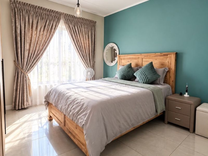 A well-maintained bedroom featuring polished tile flooring, a modern pendant light, and a striking teal accent wall, creating a bright and inviting living space.