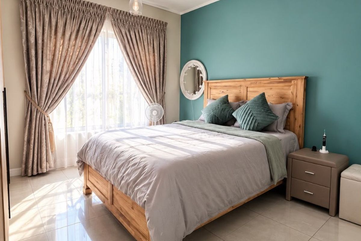 A well-maintained bedroom featuring polished tile flooring, a modern pendant light, and a striking teal accent wall, creating a bright and inviting living space.