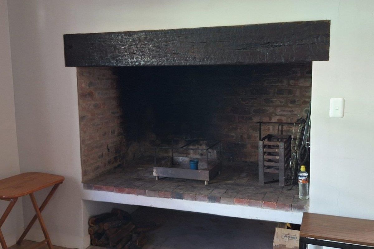 A rustic indoor fireplace featuring exposed brickwork and a heavy timber mantelpiece, providing a traditional focal point for the living area.