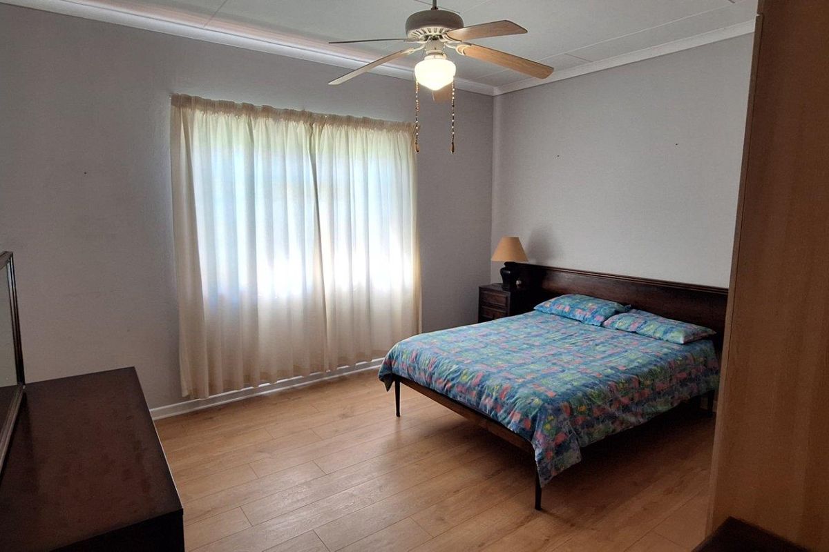 A well-lit bedroom featuring wood-look laminate flooring, a ceiling fan, and neutral wall finishes, providing a comfortable and functional living space.