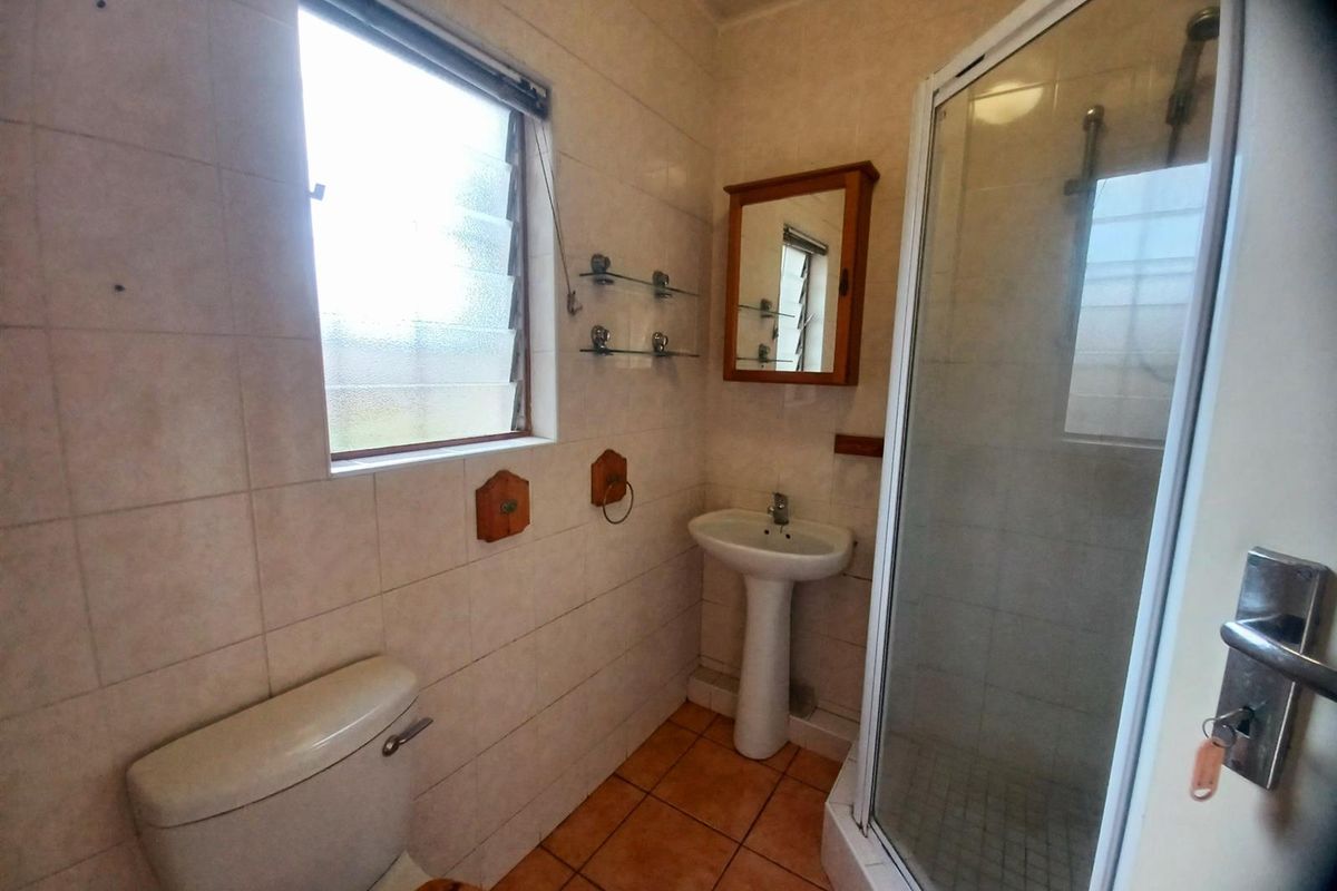 A functional bathroom featuring a pedestal basin, a shower enclosure with a glass door, and a toilet, finished with neutral wall and floor tiling.