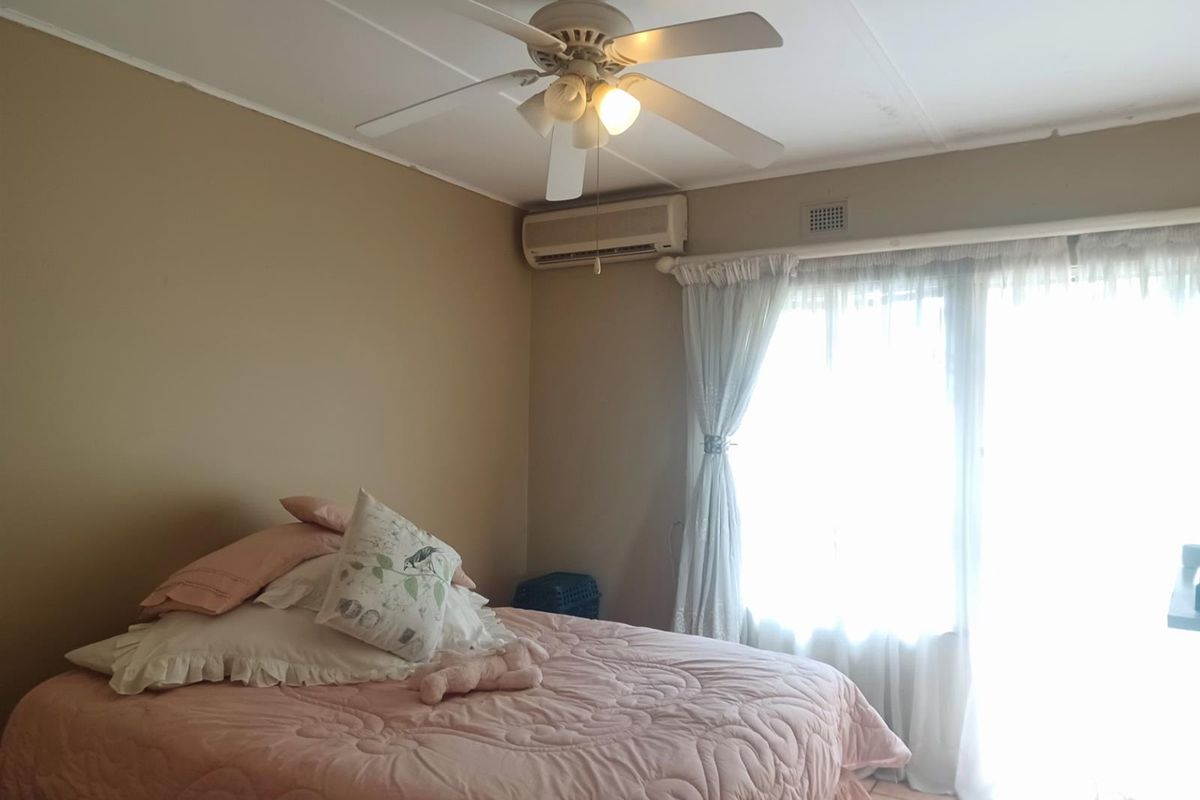 A bedroom featuring a ceiling fan, wall-mounted air conditioning unit, and large window with natural light.