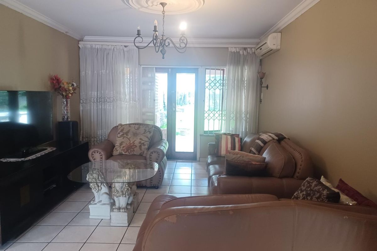 A comfortable living room featuring tiled flooring, a ceiling rose with chandelier, and direct access to the outdoor area through a security-gated door.