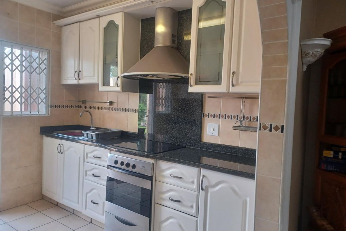 A functional kitchen featuring white cabinetry, dark granite countertops, a stainless steel extractor fan, and a built-in oven with a ceramic hob.