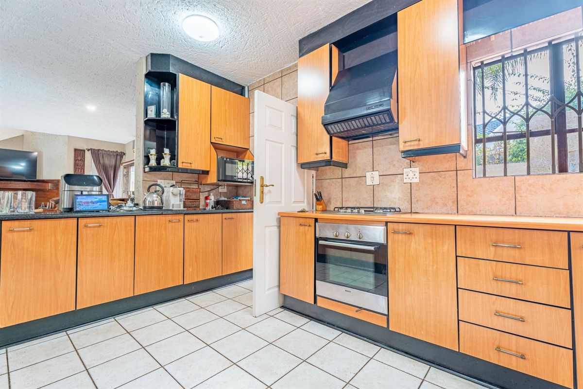 A functional kitchen featuring wood-veneer cabinetry, built-in oven, gas hob, extractor fan, and tiled flooring with a view into the adjacent living area.