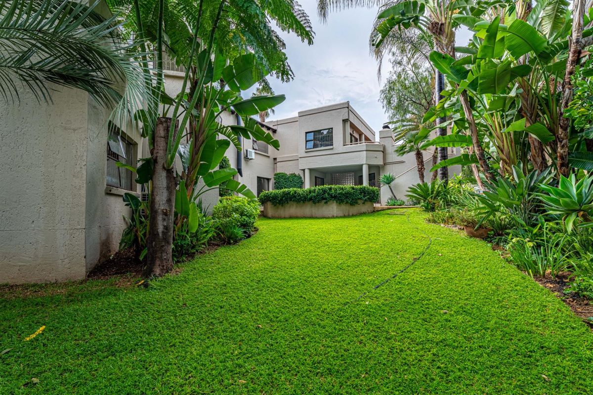 A view of the rear garden and patio area, featuring lush landscaping and a well-maintained lawn adjacent to the property's rear elevation.